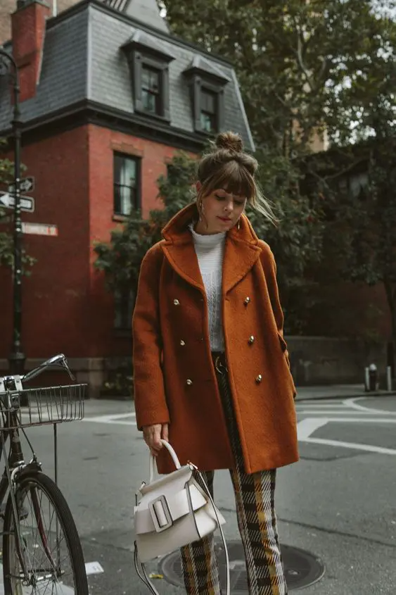 a white turtleneck, plaid trousers, a rust colored short coat, a .